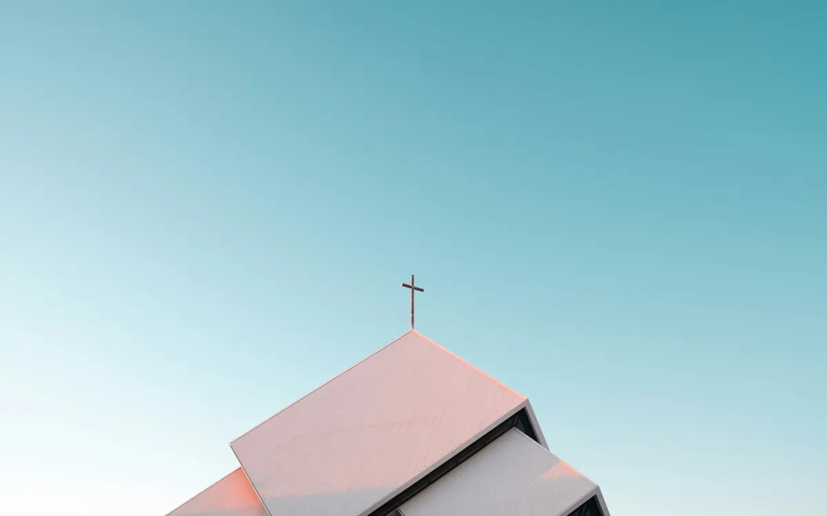 A church roof peak with a cross against a clear blue sky